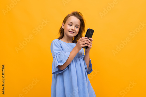 beautiful little girl on an orange background with a phone in her hands
