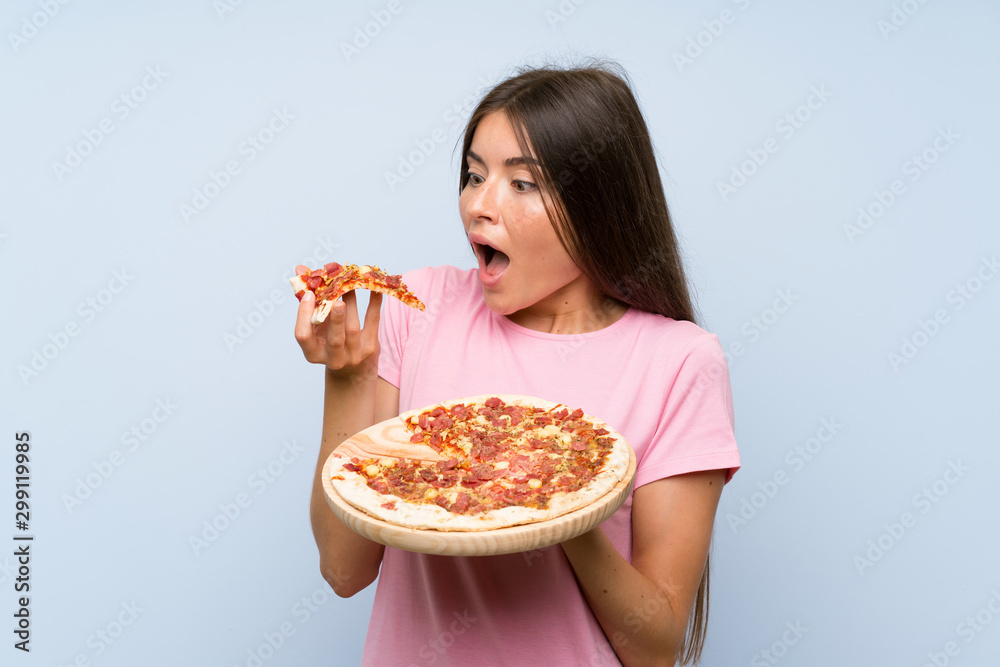 Pretty young girl holding a pizza over isolated blue wall