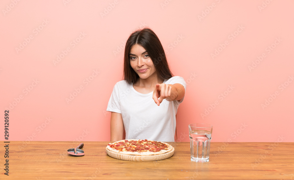 Young woman with a pizza points finger at you with a confident expression