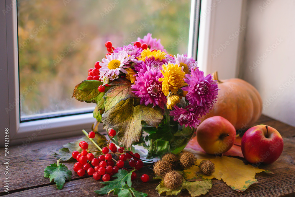 Obraz premium multicolored autumn chrysanthemum flowers in a glass vase on a wooden background.