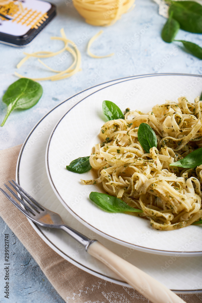 Appetizing pasta with sauce pesto and spinach in plate on light blue stone table Appetizing pasta with sauce pesto and spinach in plate on light blue stone table
