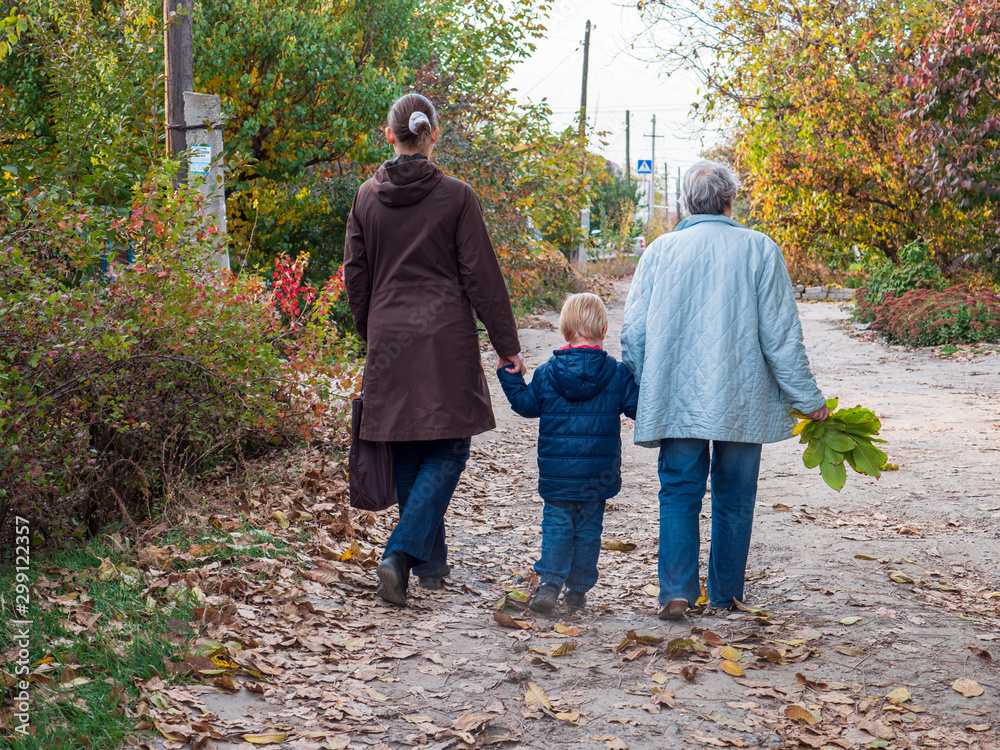 Family on walk. Grandmother, mother and child walk along alley in village. Autumn and fallen leaves