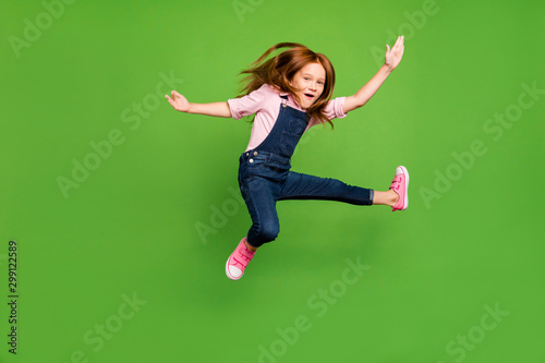 Full length photo of cheerful funny pretty little schoolchild jumping high fighting exercises training wear casual denim overall pink shirt isolated green background