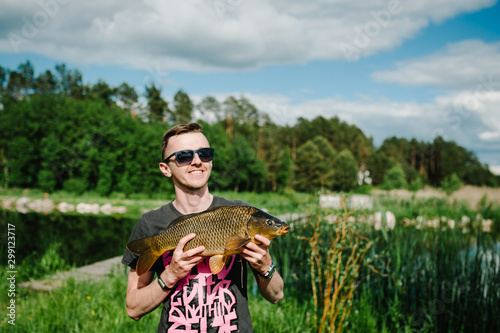 Happy cheerful young fisherman hold a big fish carp on a background of lake and nature. Fishing background. Good catch. Trophy fish. angler.