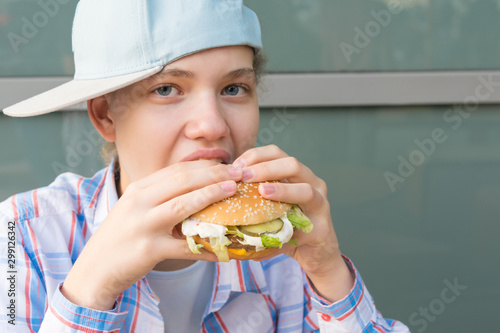 girl in a baseball cap eats a hamburger with meat  front view  close-up