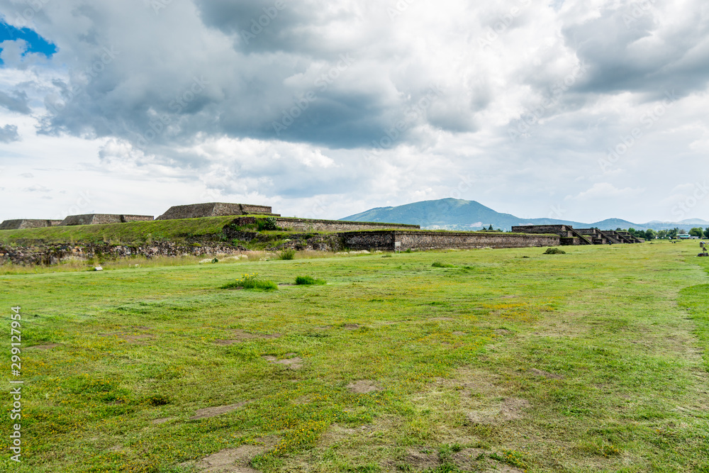 Ruins of the architecturally significant Mesoamerican pyramids and green grassland located at at Teotihuacan, an ancient Mesoamerican city located in a sub-valley of the Valley of Mexico