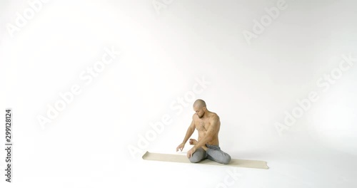 bald athlete is sitting on sporty mat and spinning torso, stretching muscles of back, legs and hands, warming body photo