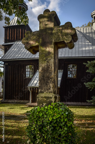 Stone cross on the background of the wooden Church of St. Lawrence (Wawrzyniec) in Grojec, Poland.  photo