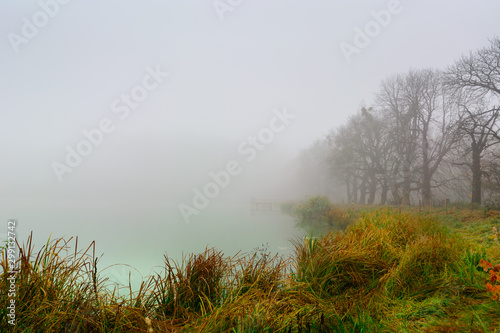Morning fog on the lake in the fall. Mystical and mysterious weather. Gray autumn natural background.