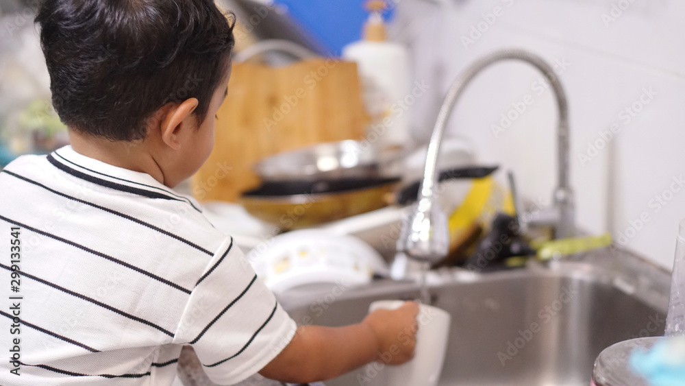 Two-year-old of Asian boy stands to wash his bottle in the kitchen alone. kid or baby help hose work on holiday concept. Two-year-old of Asian boy stands to wash his bottle in the kitchen alone. kid or baby help hose work on holiday concept.