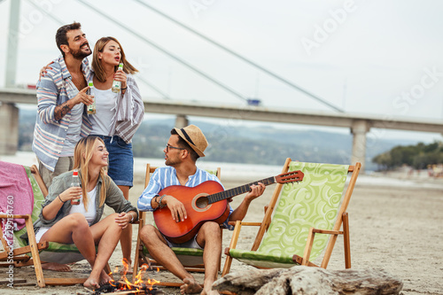 Group of friends sitting by the camp fire at the beach.they singing and play guitar.Autumn season.