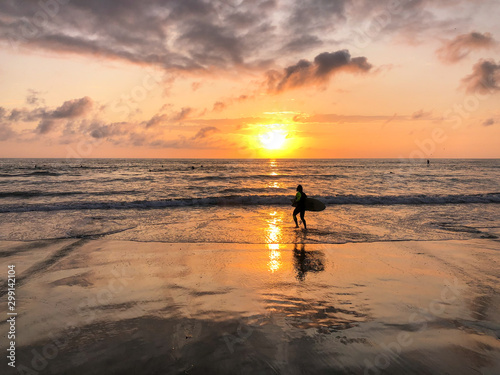 Silhouette of surfer with his board on the beach at Sunset. A man is walking with a surf in his hands across the sea shore during sunset.