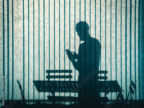 silhouette on turquoise office curtain of a standing man using his smartphone