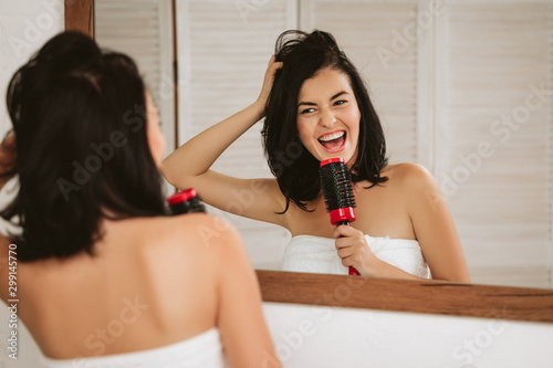 beautiful happy woman brushing healthy hair in front of the mirror. girl combing her hair and fools around