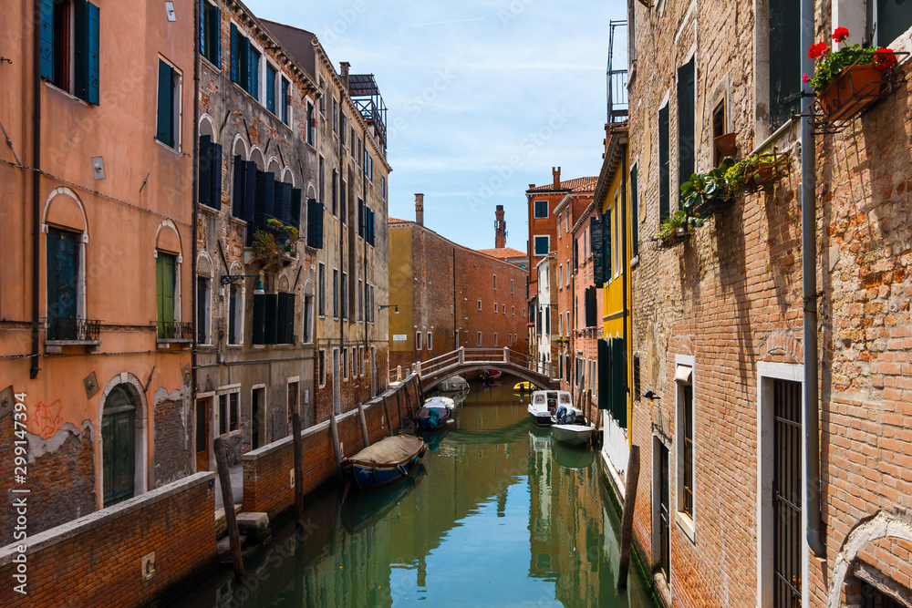 Grand Canal in Venice with boats and gandules docket motor boat near the bridge. Colorful residential house and small bridges cross the canal.