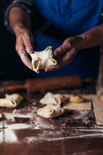 A woman is preparing buns from puff pastry oaking apple envelopes puff pastry cakesn a table in a bakery. The process of m. Seventh step, put slices of apples on the dough and form an envelope. 