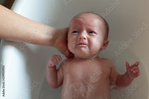 Newborn baby is being bathed by his mother. Newborn baby crying in bath time