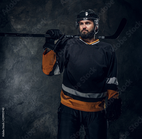 Fotografie Portrait of brutal bearded man in hockey player uniform at dark photo studio