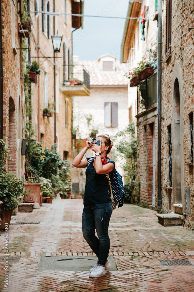 Young female traveler taking photos on the streets of an old Italian town of Pienza in Tuscany, Italy   