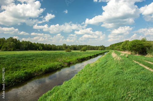 Eastern Poland and river flowing through meadow and forest, clouds on blue sky