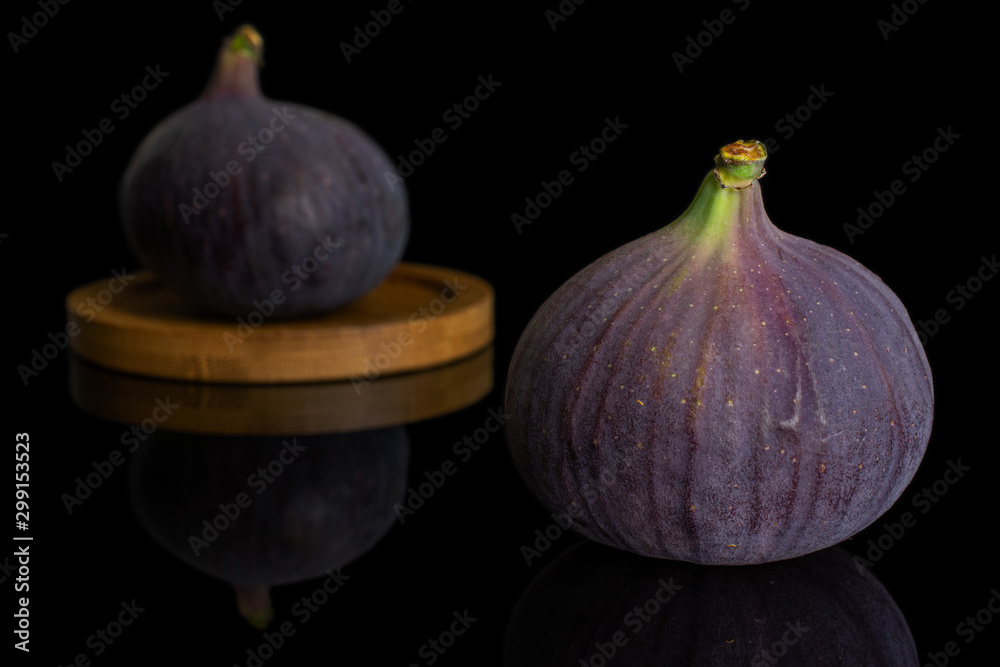 Obraz premium Group of two whole fresh purple fig on bamboo coaster isolated on black glass