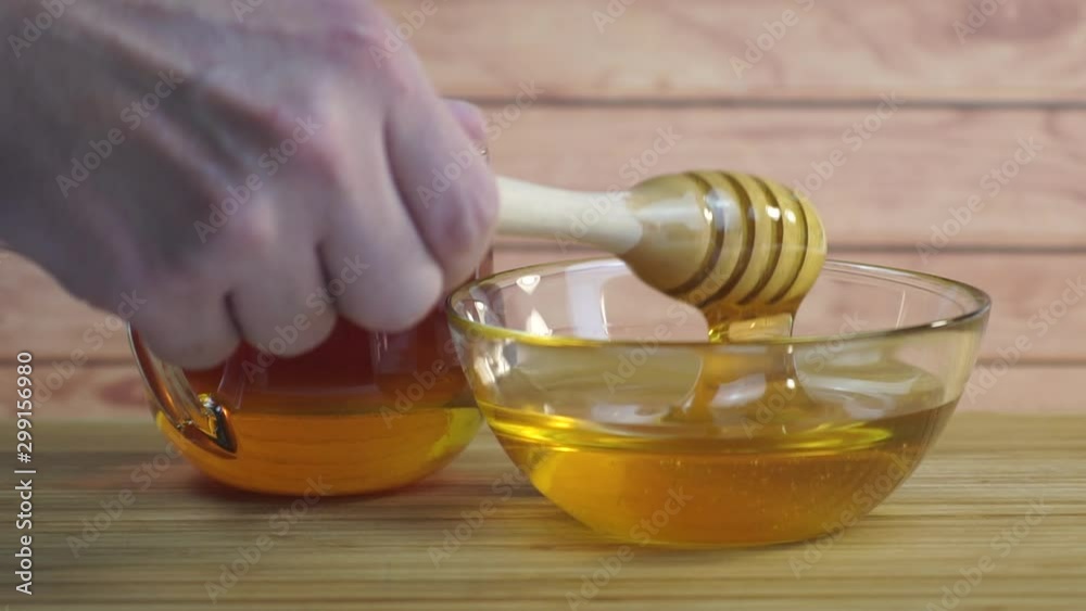 Honey dripping, pouring from dipper in glass bowl. Close-up and macro. Healthy organic thick honey dipping from the wooden honey spoon, closeup. Close-up of wooden dipper used in honey jar.