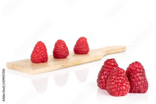 Group of six whole fresh red raspberry on small wooden cutting board isolated on white background