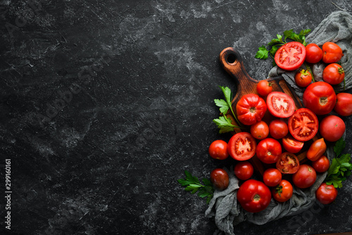 Fresh red tomatoes on black stone background. Greens. Top view. Free space for your text.