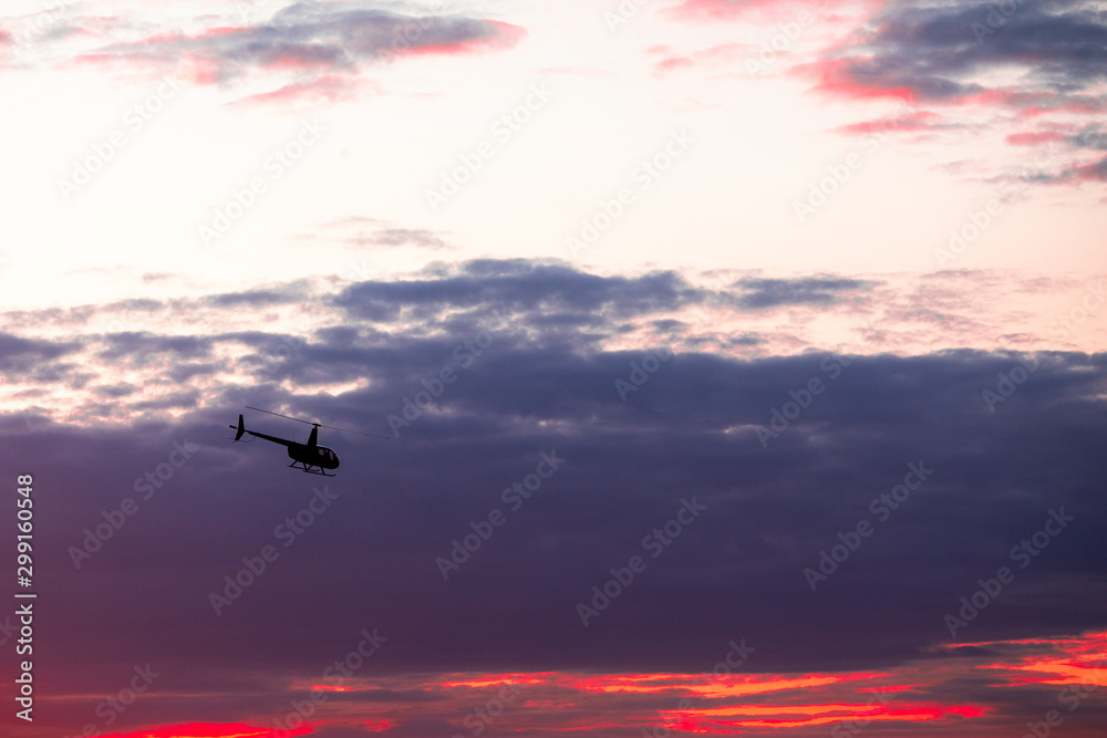 Fototapeta premium The helicopter in the astonishingly beautiful evening sky at sundown, rescue mission; aerial vehicle concept.