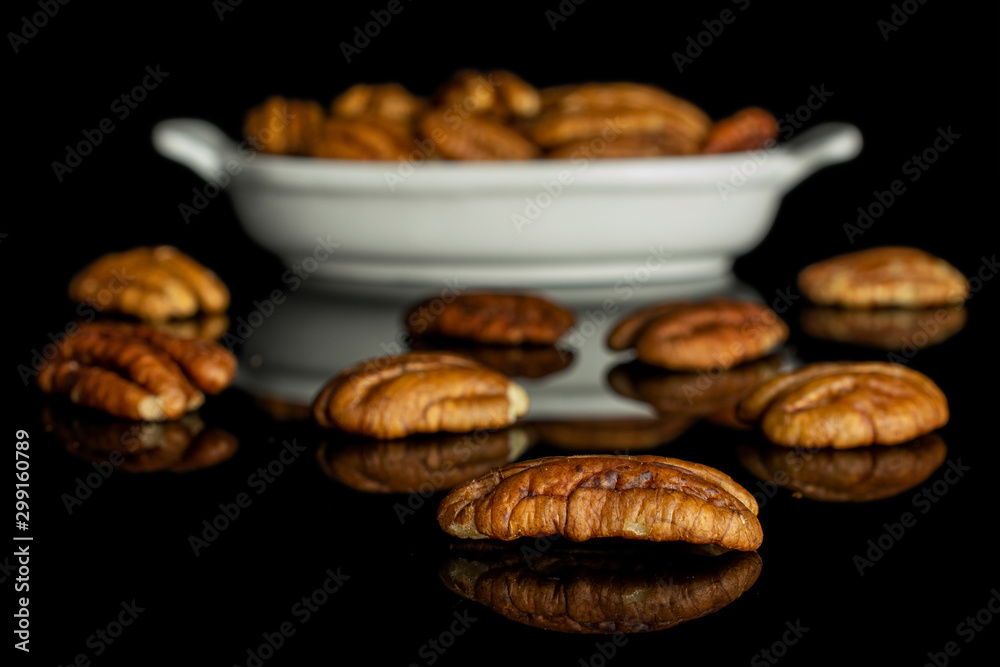 Lot of whole dry brown pecan nut in white oval ceramic bowl isolated on black glass