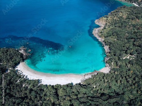 Top view of the exotic lagoon: narrow strip of the white sand framed with turquoise clear sea from one side and green tropical forest from another; paradise concept.