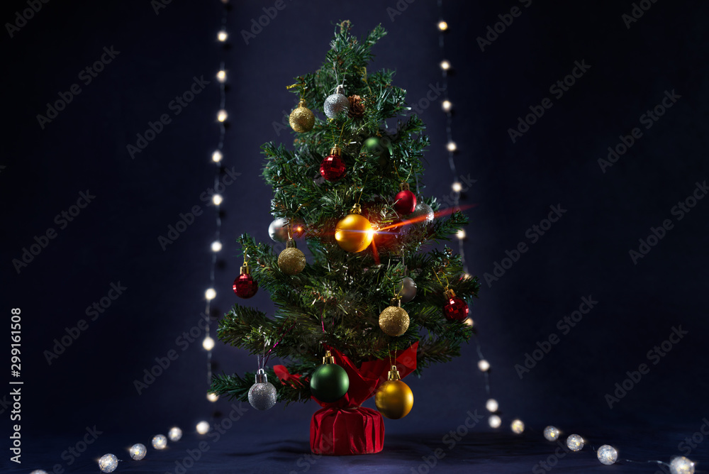 There is xmas tree with different colors ball between the glowing lights like runway.  It is on the black background. Merry Christmas. Happy New Year 2020. 