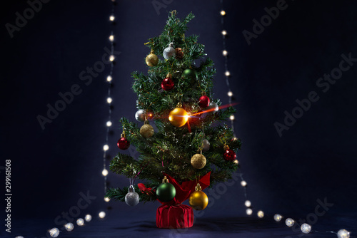 There is xmas tree with different colors ball between the glowing lights like runway.  It is on the black background. Merry Christmas. Happy New Year 2020.  © Iakov