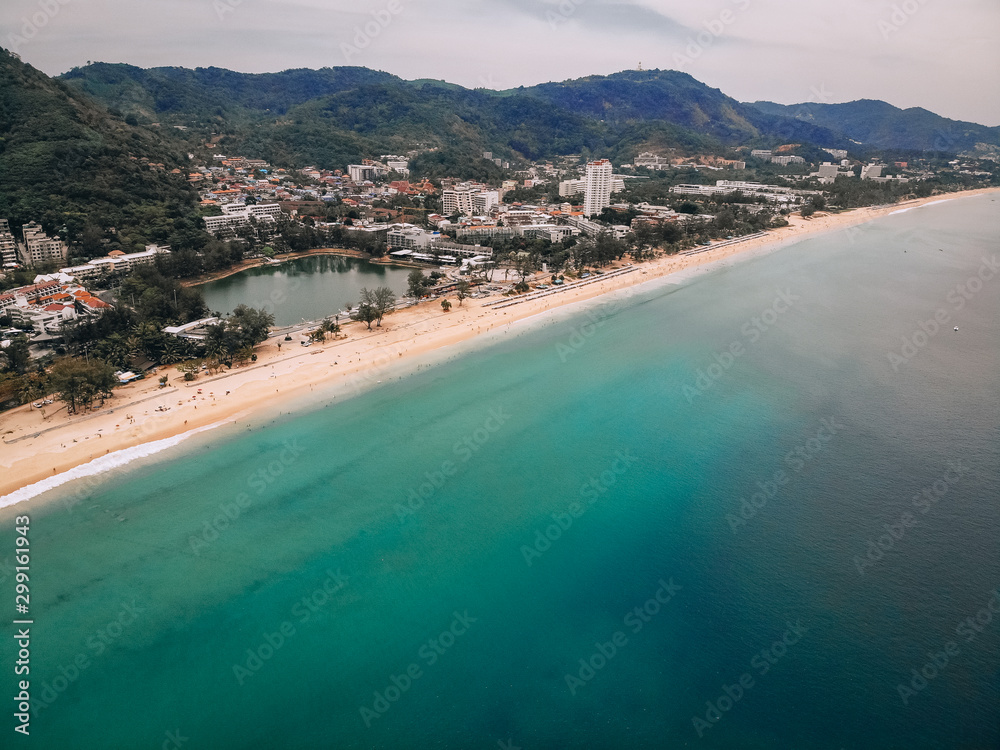Aerial view of the long sandy beach, palms, coastal town with hotels, hills and seashore; exotic country concept.