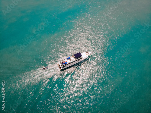 Aerial view of the speedboat and a boat behind it sailing near the coast of Thailand, white trace on the water  vessels concept. © Semachkovsky 