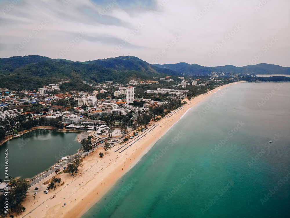 Aerial view of the long sandy beach, palms, coastal town with hotels, hills and seashore; exotic country concept.