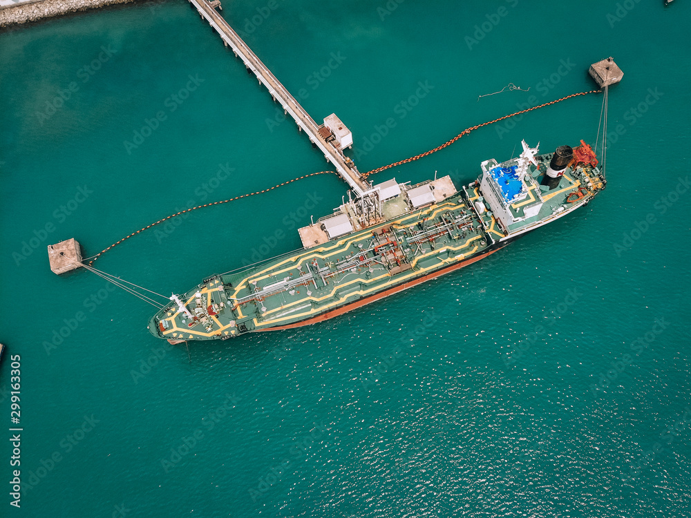 Top view of the tanker pumping fuel through the oil line to the depot terminal on the seashore; industrial concept.