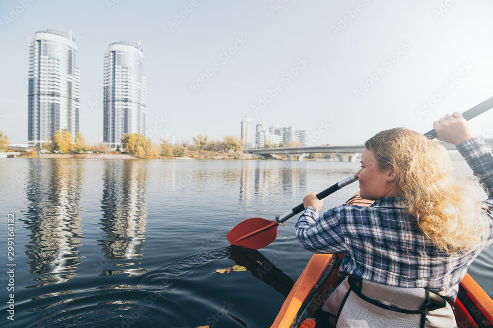 Young woman in red kayak rowing towards modern buildings on the waters of Dnipro river in Kyiv, Ukraine