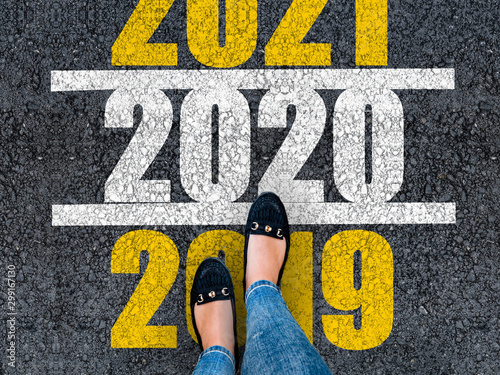 happy new year 2020. lets start 2020. woman legs in shoes walks on asphalt road next to number 2020 and 2021. She is standing on number 2019. 