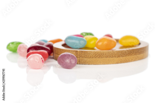Lot of whole disordered jelly bean candy on round bamboo coaster isolated on white background