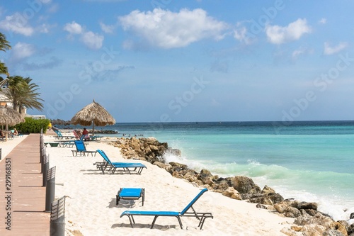 Beautiful view of sandy beach on coast line of Atlantic ocean. White sand and blue sun beds on turquoise water and blue sky with white clouds background.Aruba. Eagle Beach.