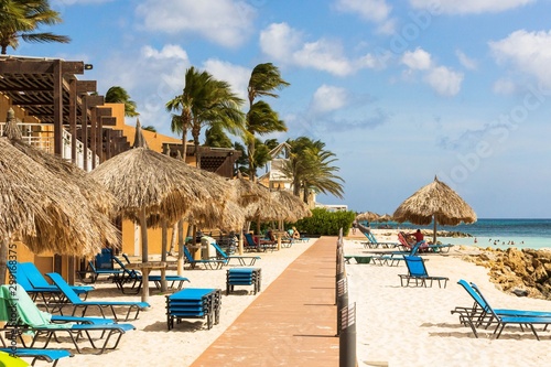 Fototapeta Naklejka Na Ścianę i Meble -  Beautiful view of sandy beach on coast line of Atlantic ocean.  White sand and blue sun beds on turquoise water and blue sky with white clouds background.Aruba. Eagle Beach.