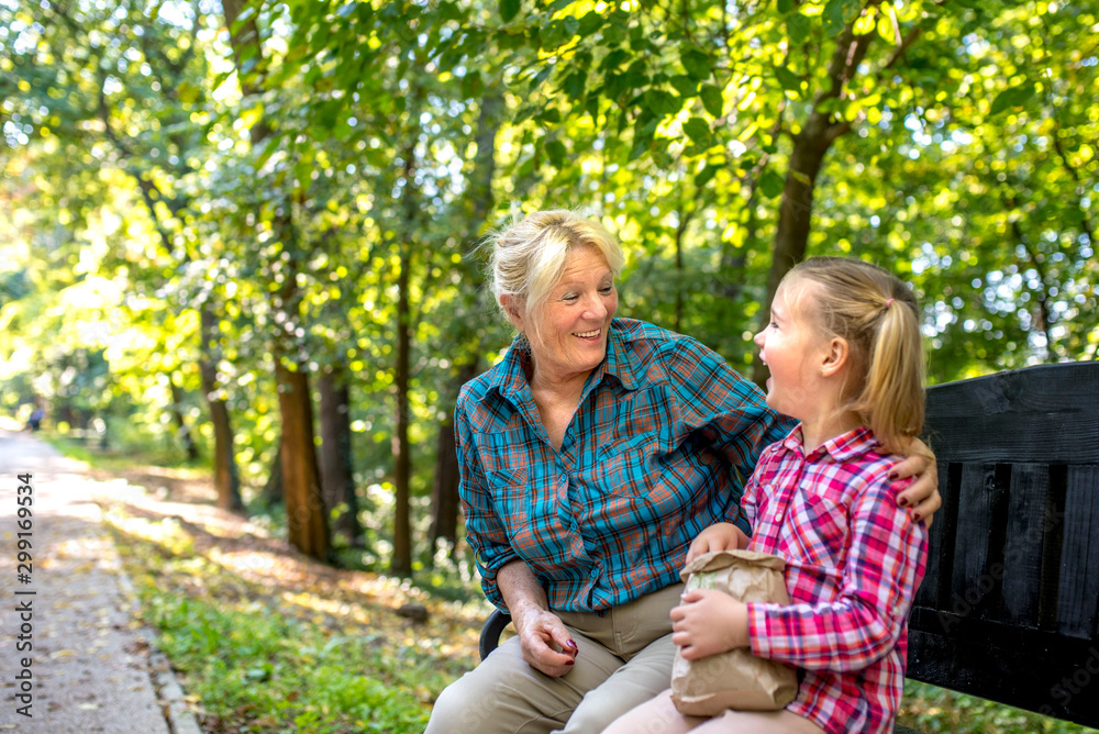 Happy grandmother and granddaughter having fun while eating popcorn in park Happy grandmother and granddaughter having fun while eating popcorn in park