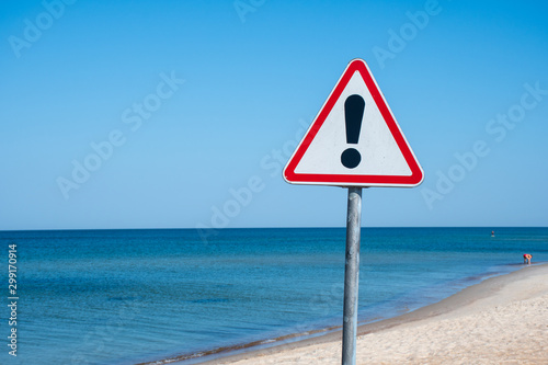 Exclamation triangle, warning sign, danger sign icon on the beach with blue sea on background, covid, coronavirus, safe beach