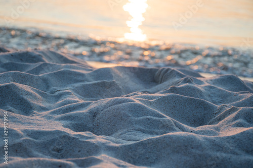 Fototapeta Naklejka Na Ścianę i Meble -  Waves of the sea meet the sand on the shore of a sandy beach on sunset, with reflection of the sun on the water, close up