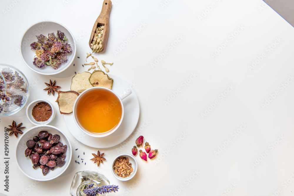 a white mug on a white table with herbal tea and herbal ingredients laid out on the table. Concept on the topic of herbal treatment for colds and flu in autumn. Top view a white mug on a white table with herbal tea and herbal ingredients laid out on the table. Concept on the topic of herbal treatment for colds and flu in autumn. Top view