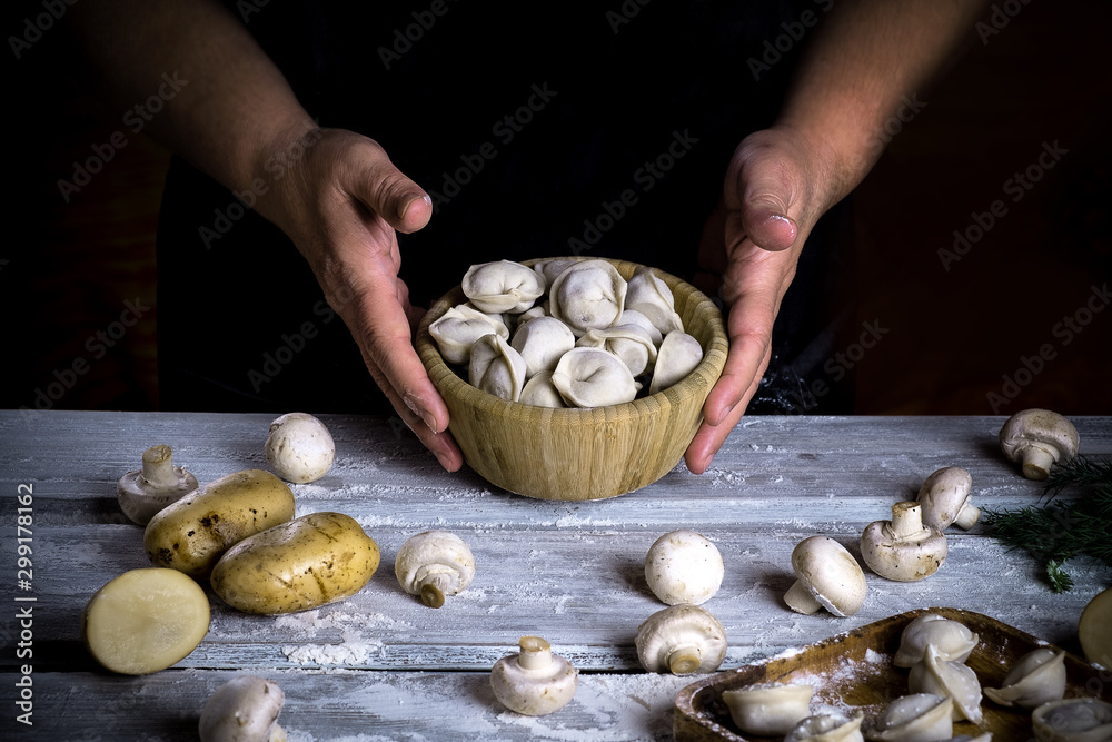 Dumplings with potatoes and mushrooms in a wooden bowl hands cook. On a wooden table ingredients. Food photography in the dark key