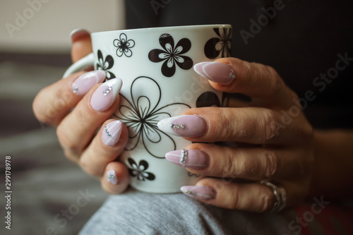 Women's hands with manicured nails holds cup of coffee