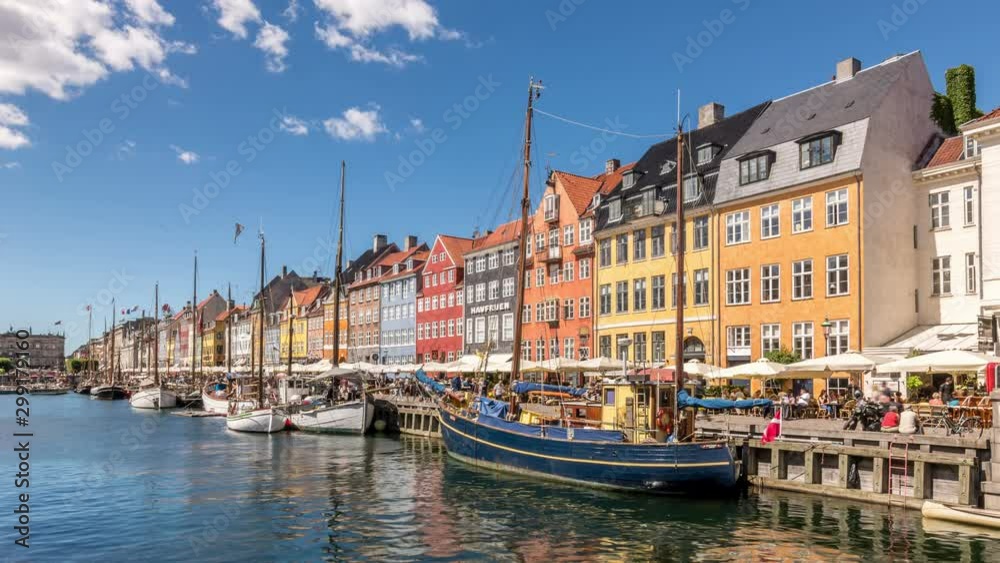 Time lapse video of Nyhavn canal (New Harbour), a 17th-century waterfront and entertainment district in Copenhagen, Denmark. Colorful houses and sailing boats. White clouds move across blue sk