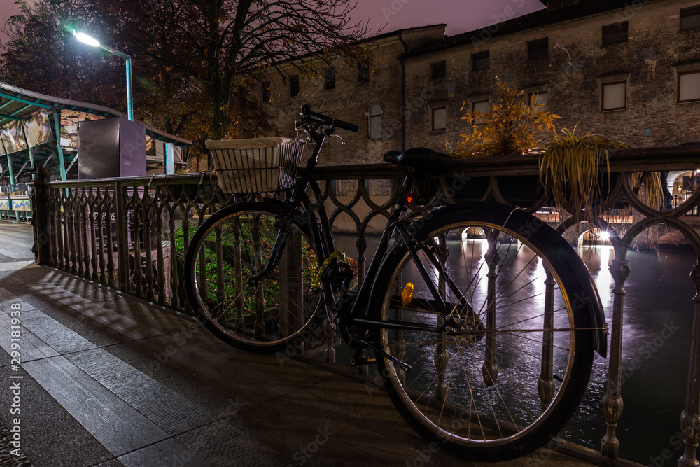 Black city bike parked on the bridge to the island of Pescheria Isola di Pescheria at night Treviso Italy